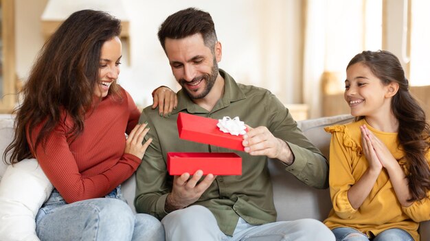 Une famille joyeuse fête la fête en donnant une boîte cadeau au père à l'intérieur