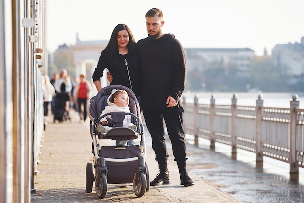 Une famille joyeuse avec un landau se promène avec son enfant dans le parc.