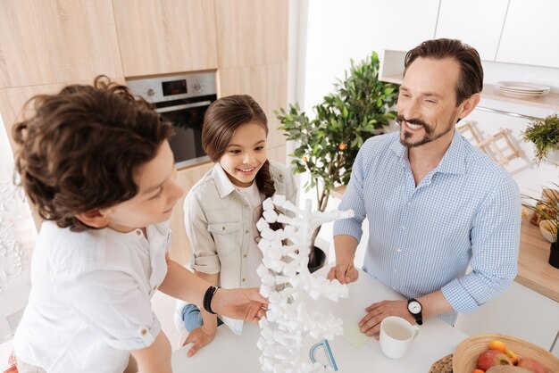 Famille joyeuse et soudée debout autour d'un grand modèle d'ADN 3D, le scrutant tout en ayant l'air inspiré et heureux d'étudier ensemble