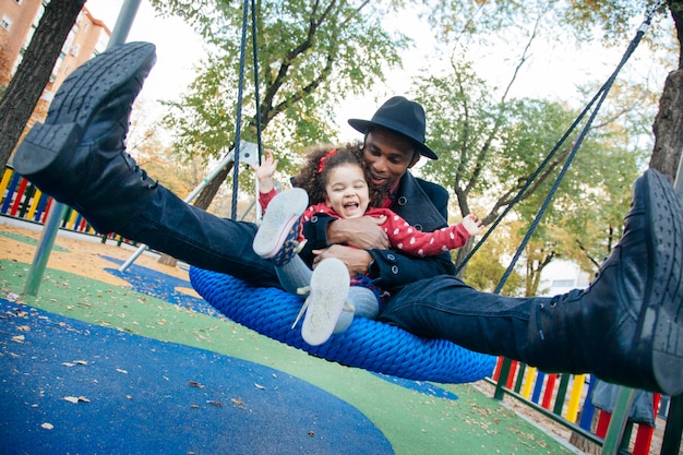 Photo famille latine se balançant dans un parc pour enfants de la rue