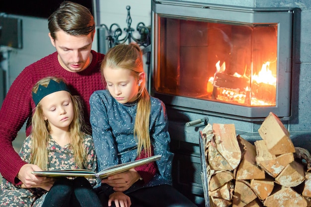 Famille Lisant Un Livre Ensemble Près De La Cheminée Le Soir De Noël