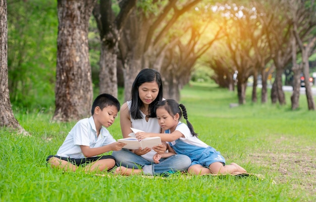 La famille lit un livre assise sur l'herbe contre les arbres.