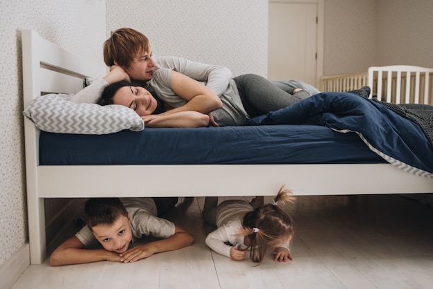 Famille à la maison en pyjama. Fille et fils. Réveillez-vous le matin. Embrassant et embrassant dans la chambre sur le lit. Enfants sous le lit. Fool around