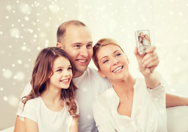 famille, maison, technologie et personnes - famille heureuse avec caméra prenant une photo sur fond de flocons de neige