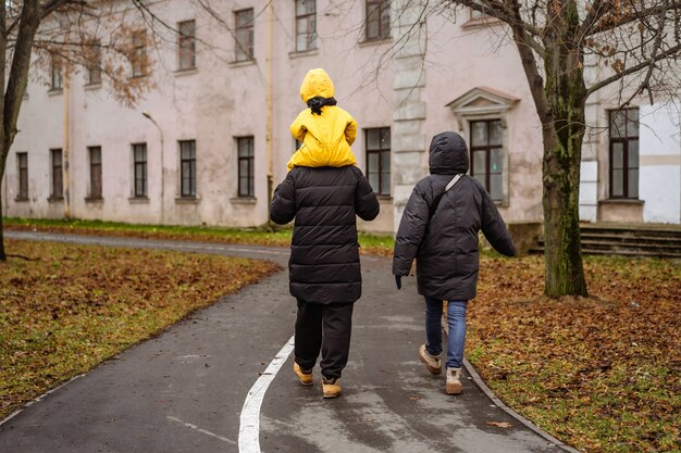 Famille marchant dans le parc. Père porte un enfant en salopette jaune sur ses shounders