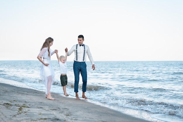 Famille marchant le long de la côte de la mer. Les parents lèvent la main de l'enfant. Concept de famille heureuse