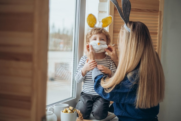 Photo famille masquée s'amusant pendant l'épidémie de coronavirus mère et fils portant des oreilles de lapin et des costumes de lapin célèbrent la pandémie de coronavirus joyeuses fêtes