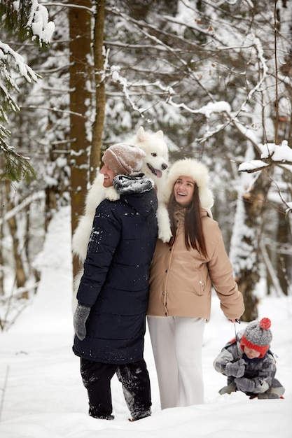 Famille de mère père et fils s'amusant dans le bois d'hiver enneigé avec un chien de compagnie joyeux