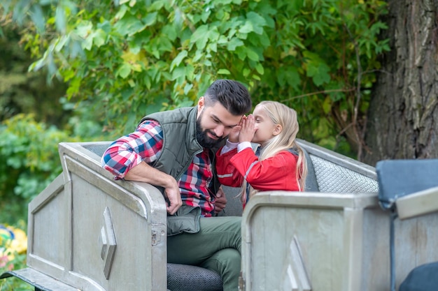 Famille mignonne. Homme brune en chemise à carreaux assis avec sa fille et à la paisible