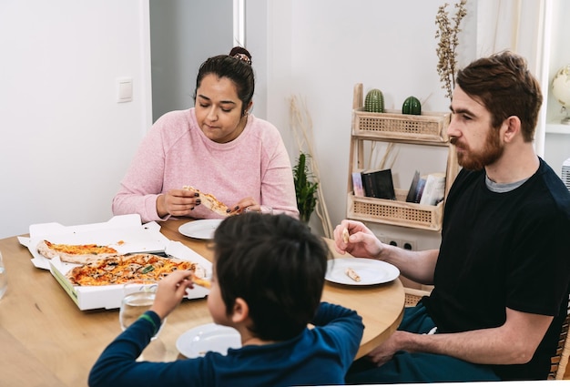 Photo une famille mixte assise à table et mangeant une pizza végétalienne avec des ingrédients naturels à la maison.