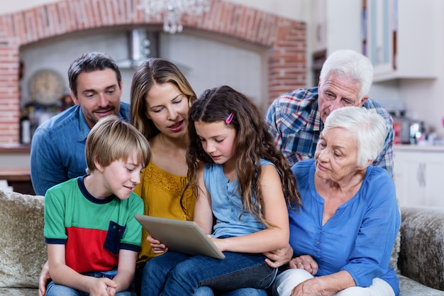 Photo famille multi-génération assise sur un canapé et utilisant une tablette numérique
