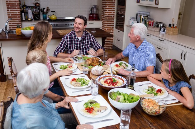 Photo famille multi-génération parlant tout en prenant son repas en cuisine