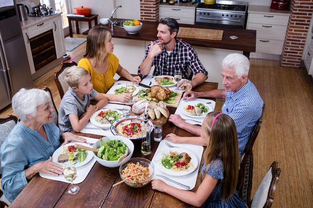 Famille multi-génération parlant tout en prenant son repas en cuisine