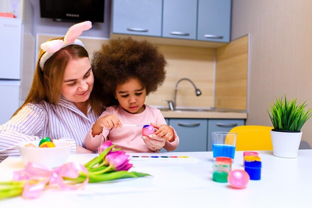 Famille multiethnique se préparant à l'événement de pâques dans la cuisine peignant des œufs