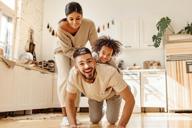 Famille multiraciale heureuse parents divers jouant avec son fils dans une cuisine confortable le week-end à la maison