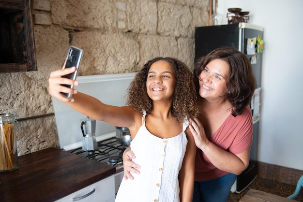 Famille multiraciale prenant un selfie dans la cuisine de leur maison