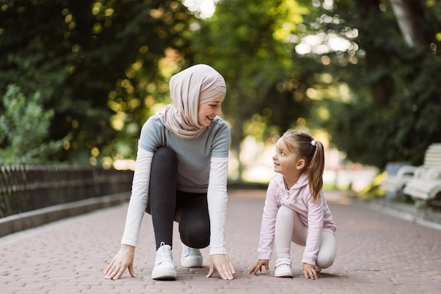 Famille musulmane active mère et fille agenouillées prêtes à commencer à faire du jogging sur la piste du parc