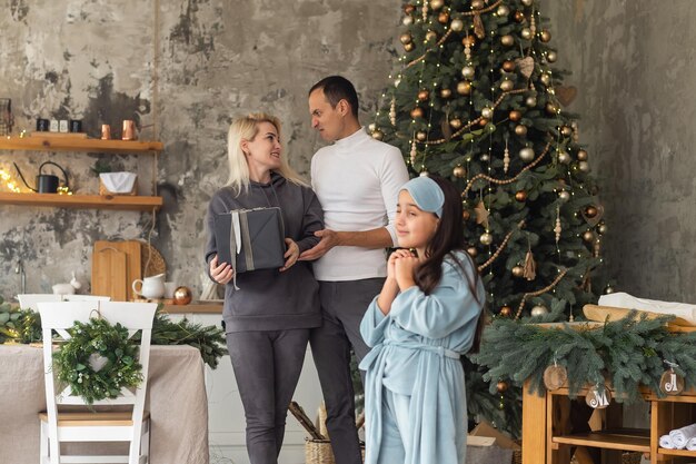 Famille de Noël. Bonheur. Portrait de papa, maman et fille à la maison près de l'arbre de Noël, tous sourient.