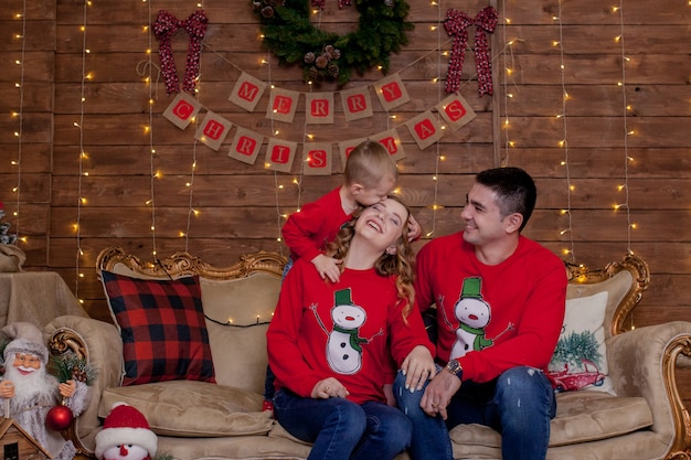 Famille de Noël. Bonheur. Portrait de papa, maman et fils assis sur un canapé à la maison près de l'arbre de Noël, tous sourient. Le concept de vacances d'hiver en famille.