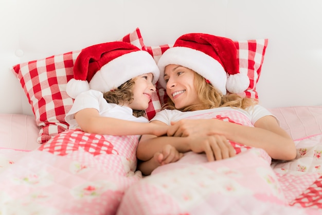 Famille à Noël Santa hats allongé sur le lit. Mère et fille s'amusant dans la chambre