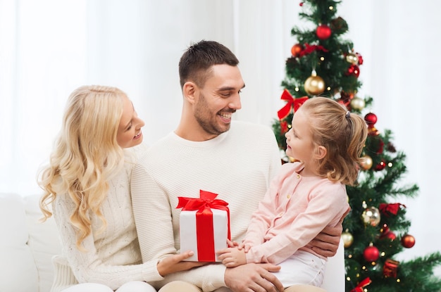 famille, noël, vacances et concept de personnes - heureuse mère, père et petite fille avec boîte-cadeau assis sur un canapé à la maison