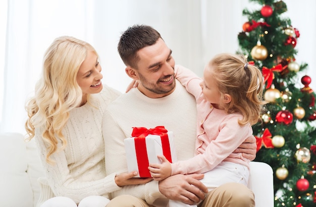 famille, noël, vacances et concept de personnes - heureuse mère, père et petite fille avec boîte-cadeau assis sur un canapé à la maison