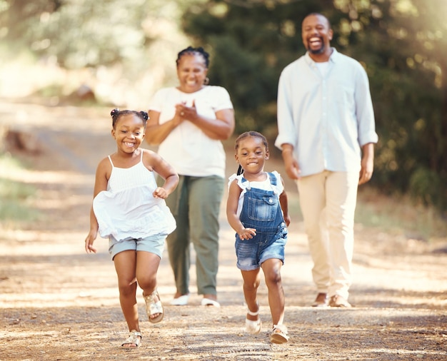 Une famille noire heureuse et des enfants qui courent dans un parc naturel en été alors que maman et papa encouragent leurs jeunes enfants africains à jouer au mode de vie et à des parents actifs marchant dans une forêt avec leurs filles en bonne santé
