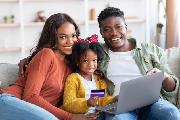 Famille noire heureuse avec ordinateur portable et carte de crédit relaxante à la maison