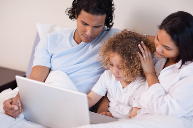 Famille avec ordinateur portable assis sur le lit