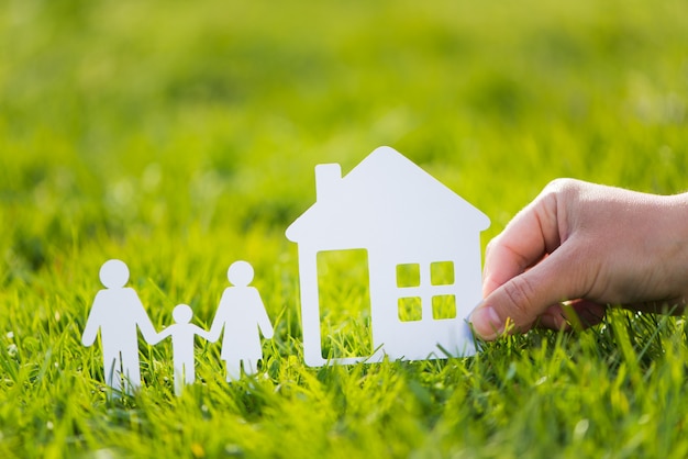 Famille de papier découpé avec maison dans l'herbe verte