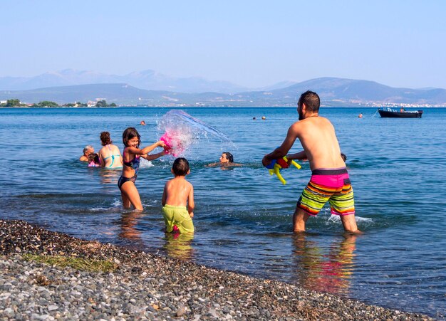 Famille père fille et fils jouent et versent de l'eau sur la plage sur une île grecque un jour d'été