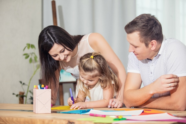 Famille père mère fille ensemble belle et heureuse à la maison ensemble dessiner des cartes