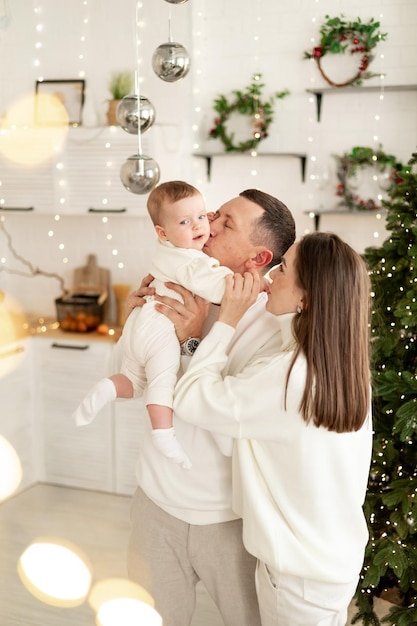 une famille avec un petit enfant profite de la nouvelle année à l'arbre de Noël dans la cuisine ou dans une maison lumineuse souriant s'embrassant et s'étreignant se félicitant les uns les autres célèbre la fête du Nouvel An