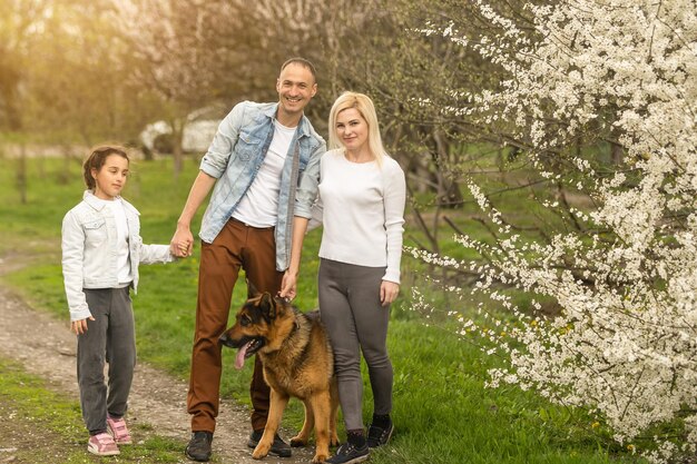 Famille avec petite fille et chien marchant à l'extérieur dans un verger au printemps