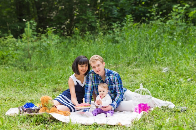 Famille en pique-nique à la journée ensoleillée. Heureuse famille métisse ayant un pique-nique et jouant dans le parc.