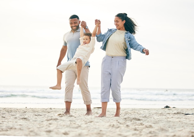 Famille à la plage et main dans la main en plein air pour la liberté de voyager et les liens dans la nature ensemble Aimez le plaisir et le garçon enfant avec de jeunes parents à la mer avec un jeu de balançoire et heureux en voyage de vacances à l'océan