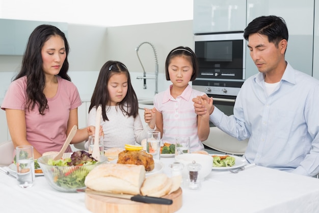 Famille de quatre disant grâce avant le repas dans la cuisine