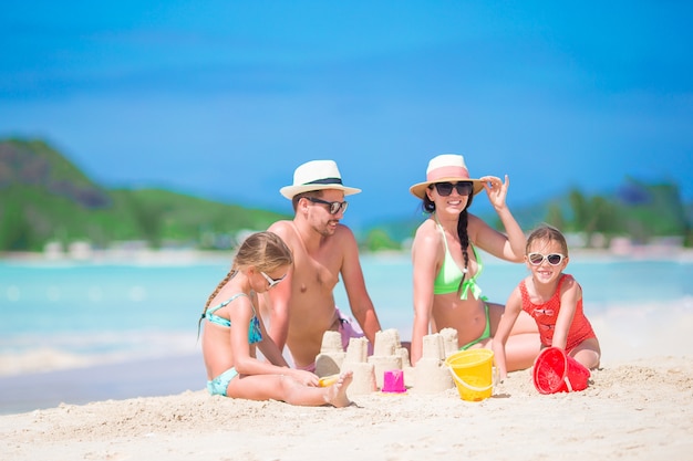 Famille de quatre faisant château de sable à la plage blanche tropicale