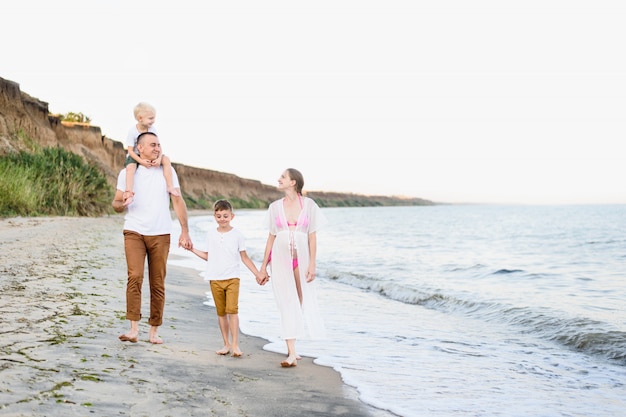 Famille de quatre personnes marchant le long du bord de mer. Parents et deux fils. Heureuse famille sympathique