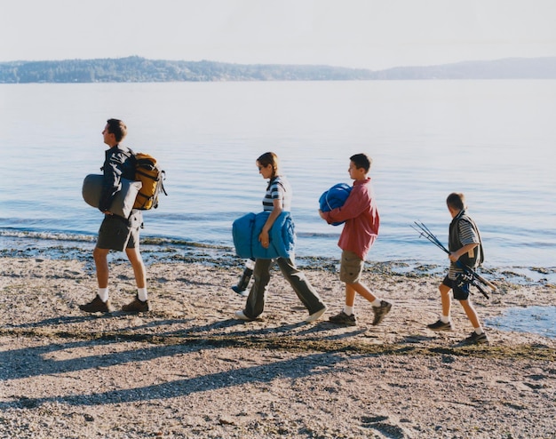Famille de quatre personnes transportant du matériel de camping marchant sur la plage au crépuscule