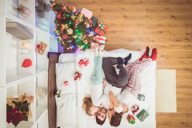 La famille qui s'embrassait était allongée sur le lit avec des cadeaux. vue d'en-haut