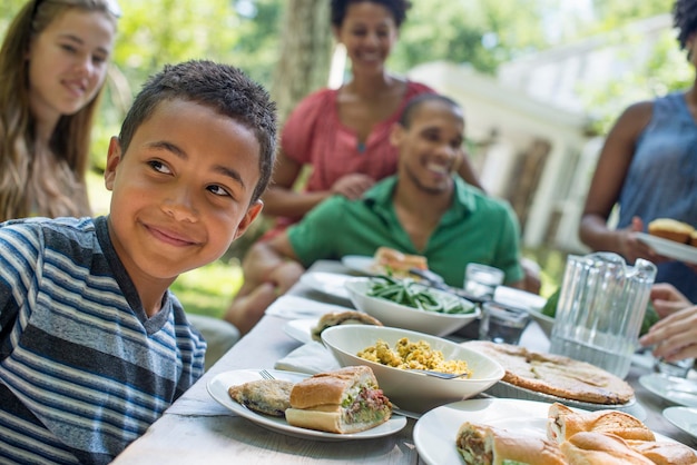 Une famille rassemblant hommes femmes et enfants autour d'une table dans un jardin en été Un garçon souriant dans le