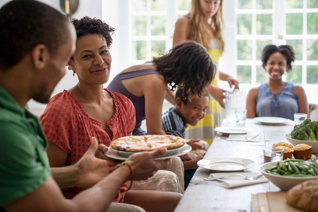 Une famille rassemblant hommes femmes et enfants autour d'une table à manger partageant un repas