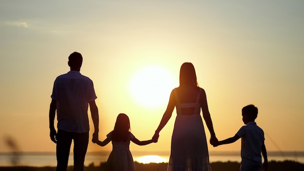 La famille regarde le coucher du soleil tenant des mains sur le pré