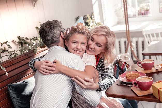 Famille de rêve. Jolie fille positive souriant tout en serrant ses parents dans ses bras