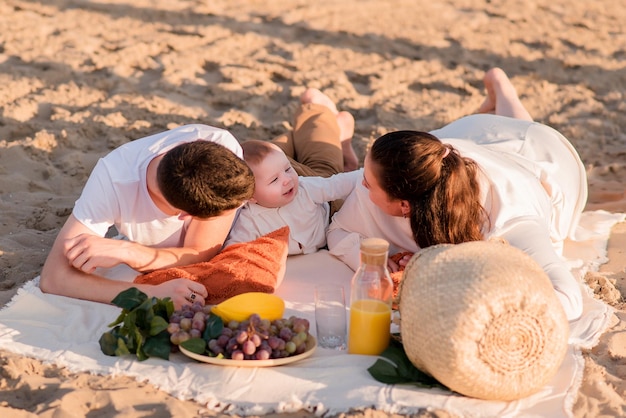 Famille se reposant sur un pique-nique sur la plage près de la mer océan mère et père tiennent un enfant une famille heureuse