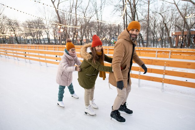 Famille se tenant l'un à l'autre en patinant sur la patinoire du parc