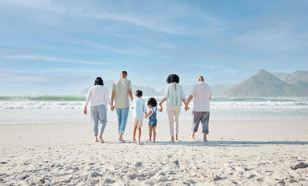 Famille se tenant la main et marchant en plein air sur une plage avec amour et bonheur pendant les vacances d'été Derrière l'espace dans le ciel ou voyager avec des hommes, des femmes et des enfants ensemble pour une aventure de vacances