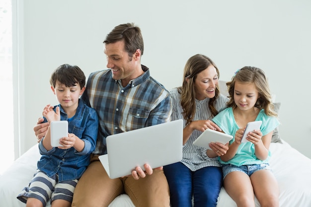 Famille souriante à l'aide d'un ordinateur portable, d'une tablette numérique et d'un téléphone portable dans la chambre