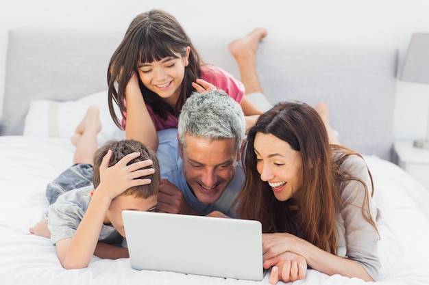 Famille souriante allongée sur le lit en utilisant leur ordinateur portable